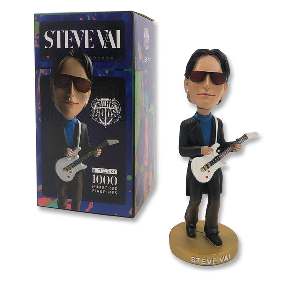 Image of a steve vai bobble head and bobble head box against white background. The bobble head is steve vai wearing black sunglasses and wearing black pants and a jacket with a blue shirt. he holds a white guitar. the stand says steve vai in white text. the box says steve vai in white text across the top and shows a photo of the bobble head. 