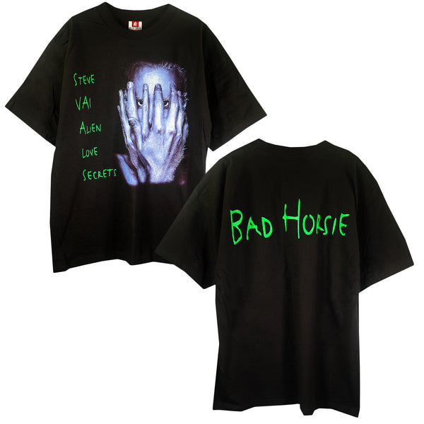 The Steve Vai Black T-Shirt features a graphic of a person covering their face with green "Alien Love Secrets" text. The back displays bold green "Bad Horsie" text—perfect for fans of Steve Vai.