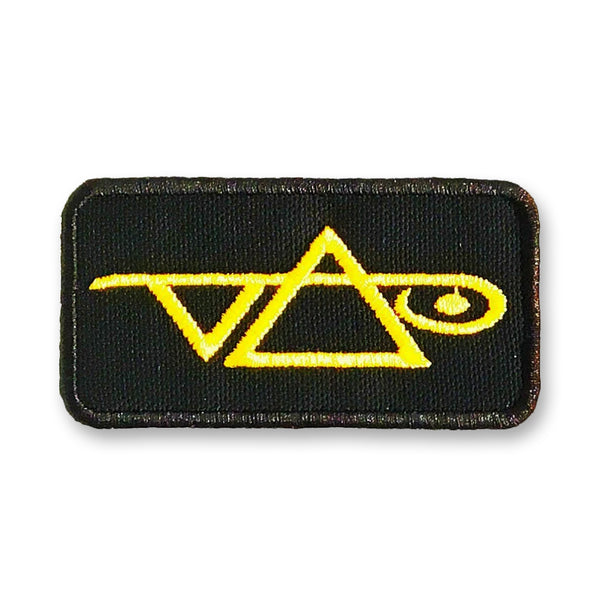 Image of a black patch against white background. the patch has a gold steve vai logo on it. The steve vai logo makes the word "vai" with an upside down triangle, a right side up one, and a line going across the triangles with a curl at the end next to the triangle that is upright. 