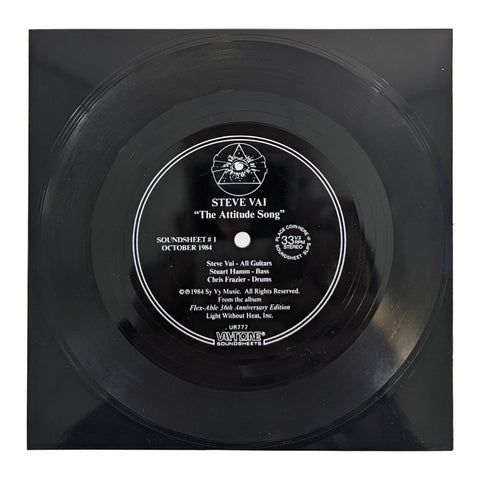 image of a black flexi vinyl record against white background. the black flexi has a black and white sticker in the middle that says "steve vai, the attitude song", along with various other information such as 33rpm playing speed, the record label, and the copyright info.