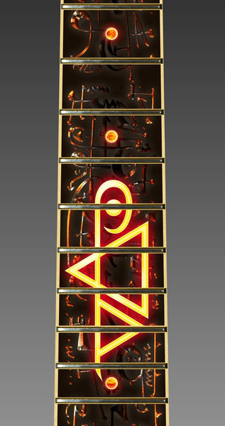 close up image of fret protector. it is black with red and orange abstract symbols. descending down the fret protector in a glowing red/orange/yellow color is the steve vai logo.  The steve vai logo makes the word "vai" with an upside down triangle, a right side up one, and a line going across the triangles with a curl at the end next to the triangle that is upright. 