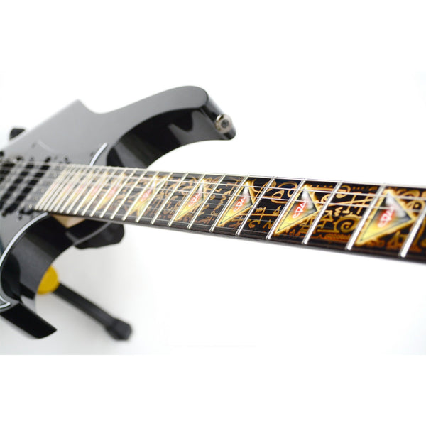close up image of a guitar against a white background. there is a fret protector on the guitar. It is black with light brown symbols all over it. Every other fret has a brown, black and greenish triangle on it with a white steve vai logo in the center of it. The steve vai logo makes the word "vai" with an upside down triangle, a right side up one, and a line going across the triangles with a curl at the end next to the triangle that is upright. 