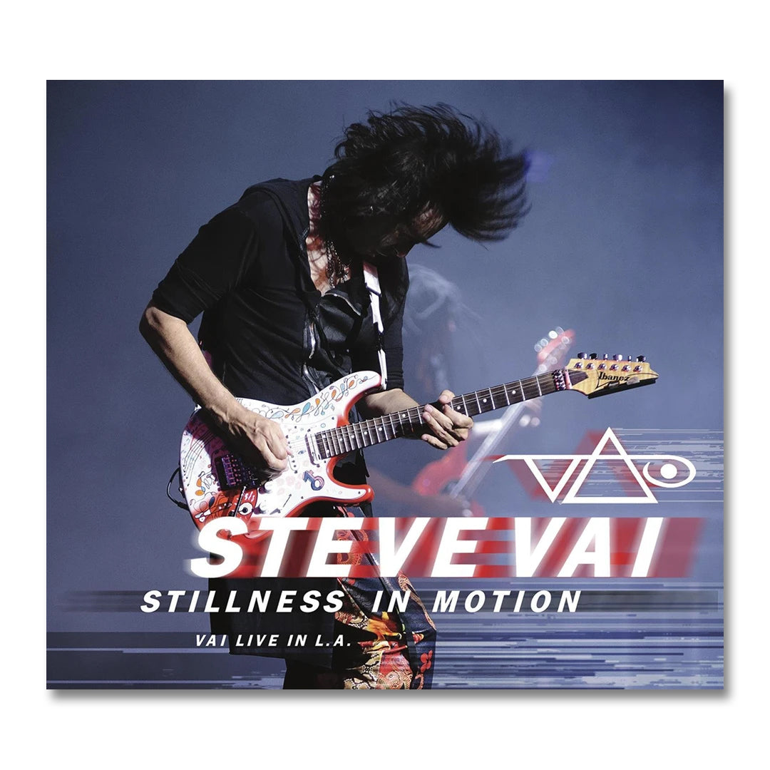 steve vai stillness in motion album artwork. steve vai plays electric guitar against a grey and blue background. his hair is flipped up in the air. below steve in red and white text reads "steve vai, stillness in motion, vai live in LA". the steve vai logo in red and white is above this text. the logo  makes the word "vai" with an upside down triangle, a right side up one, and a line going across the triangles with a curl at the end next to the triangle that is upright. 