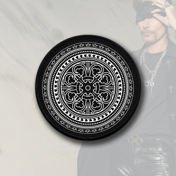  Image of a black and white circular patch against a faded white transparent background with an image of steve vai in the corner lifting a bandana up that is over his eye. the patch is black and has white print on it. it is an abstract circular image that has a pattern made up of various shapes and symbols that makes it look like it moves when you look at it.