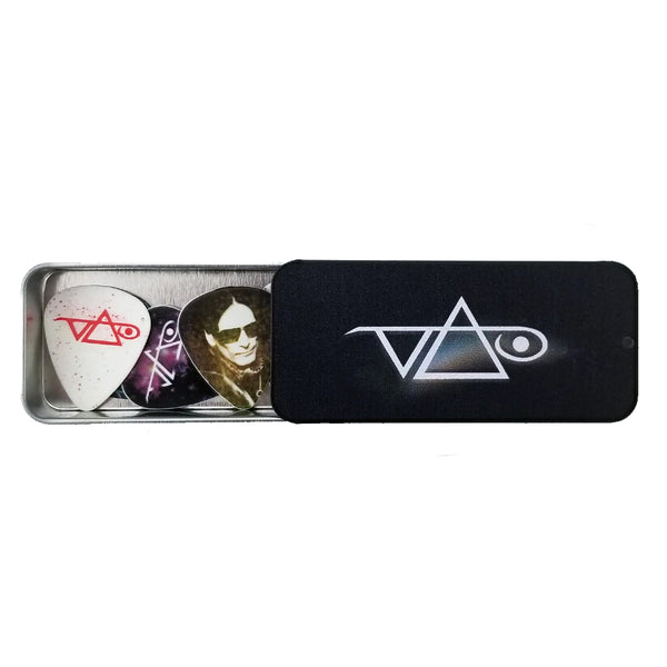  image of a black guitar pick tin with guitar picks in it against white background. the tin is black with a white steve vai logo in the center. The steve vai logo makes the word "vai" with an upside down triangle, a right side up one, and a line going across the triangles with a curl at the end next to the triangle that is upright. the guitar picks are an assortment of different ones-silver with a red steve vai logo, a photo of steve vai, and a galaxy print with a white steve vai logo on it.