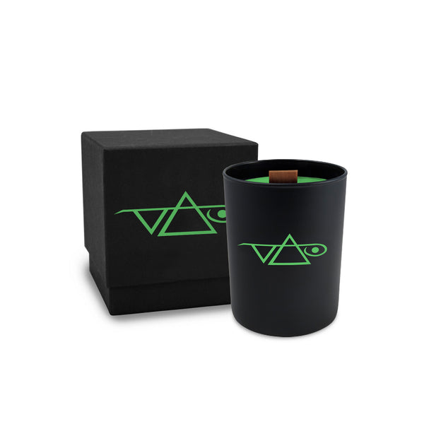  Image of the front of a black candle with the candle box against white background. The front of the candle has a green steve vai logo that makes the word "vai" with an upside down triangle, a right side up one, and a line going across the triangles with a curl at the end next to the triangle that is upright. The candle box is black and features this same logo, in the same green color.