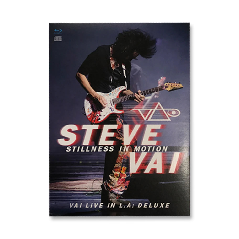 steve vai stillness in motion album artwork. steve vai plays electric guitar against a grey and blue background. his hair is flipped up in the air. below steve in red and white text reads "steve vai, stillness in motion, vai live in LA: deluxe". the steve vai logo in red and white is above this text. the logo makes the word "vai" with an upside down triangle, a right side up one, and a line going across the triangles with a curl at the end next to the triangle that is upright.