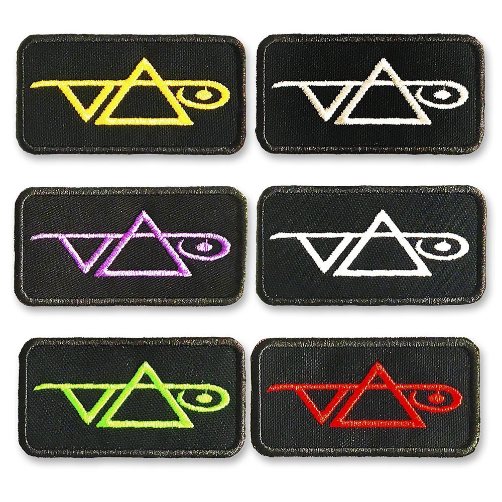 Image of 6 black rectangular patches against white background. Each patch has the steve vai logo on it, one in yellow, two in white, one in pink, one green, and one red.  The steve vai logo makes the word "vai" with an upside down triangle, a right side up one, and a line going across the triangles with a curl at the end next to the triangle that is upright. 